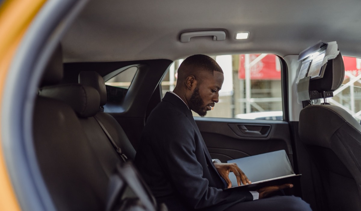 A passenger working on a laptop in the back seat of a car