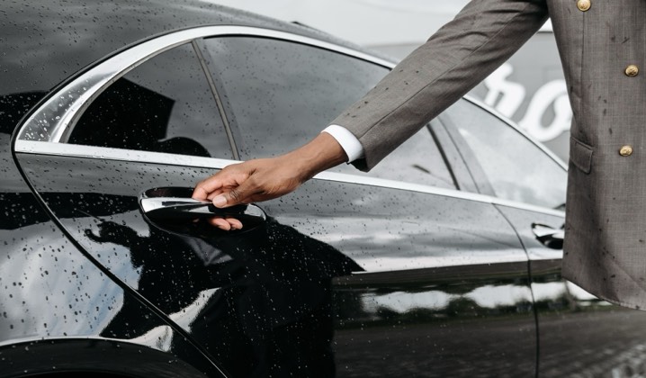 A chauffeur's hand on the door handle of a black sedan
